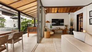 A modern living room with a sofa, a dining table with chairs, a TV, and a small table with decorative items.