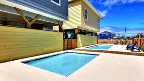 A residential area with two swimming pools, wooden fences, and a blue house in the background. - Shared Pool, Golf Cart Access, Pet Friendly (Port Aransas)