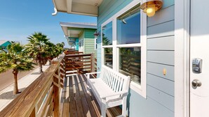 A wooden deck with a white bench, a metal door with a keypad, and a wall-mounted light fixture. - Shared Pool, Golf Cart Access, Pet Friendly (Port Aransas)