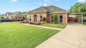A single-story brick house with a front yard, a driveway, and a covered patio area.
