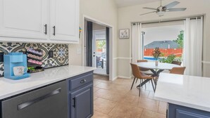 A kitchen with white cabinets, a coffee station, and a dining area with a table and chairs.