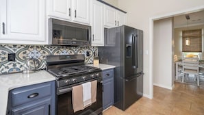 A kitchen with white cabinets, a stainless steel refrigerator, a stove, and a microwave.