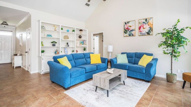 A living room with two blue sofas, a coffee table, a bookshelf, and a potted plant.