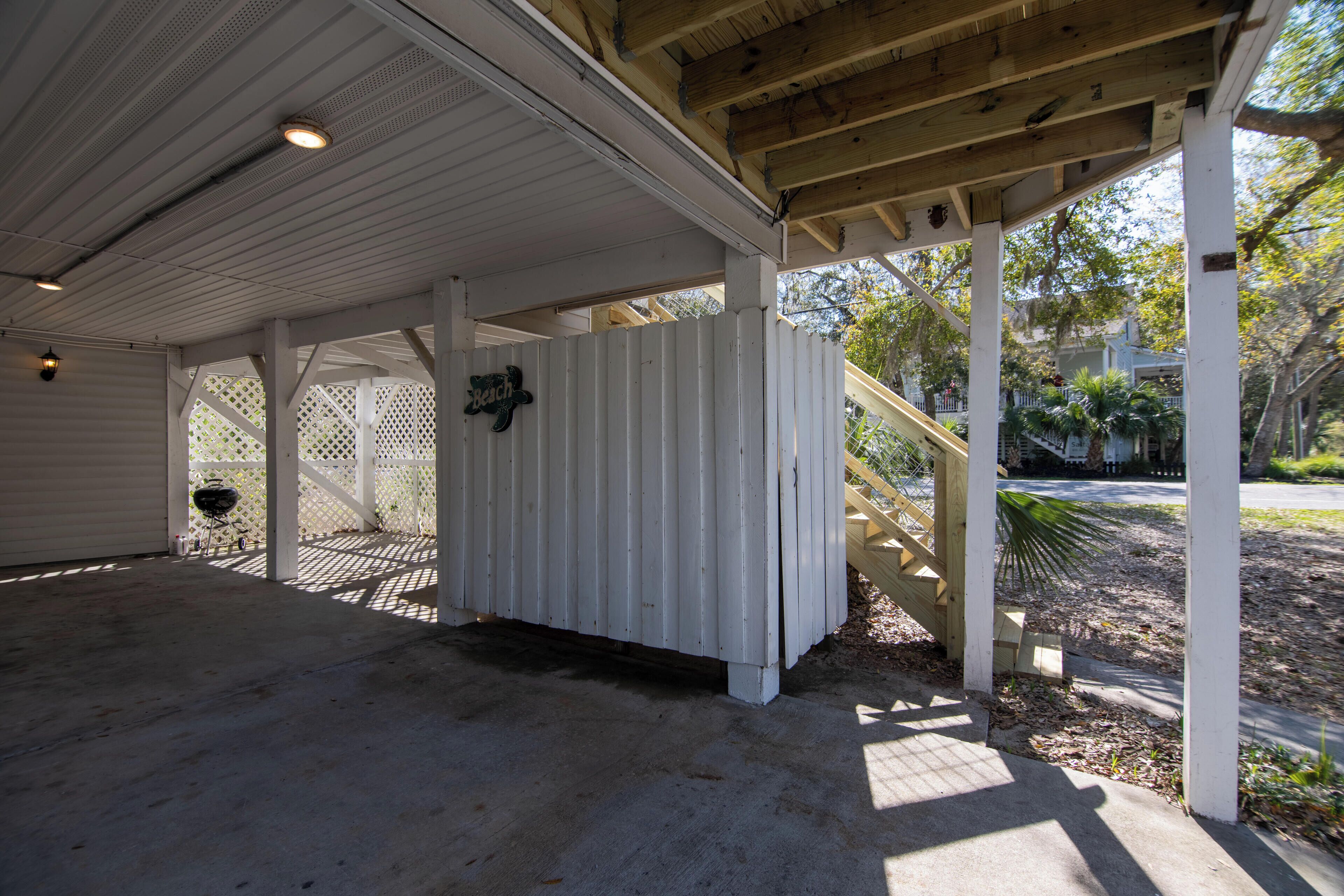 A covered outdoor area with a concrete floor, wooden beams, and a white fence.