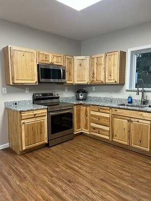 Eine Küche mit Holzausstattung, Mikrowelle aus Edelstahl, Backofen und einer Arbeitsplatte aus Granit.
