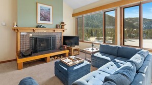 A cozy living room with a fireplace, a large window offering a mountain view, and a comfortable blue sofa. - L1740-2 (Keystone)