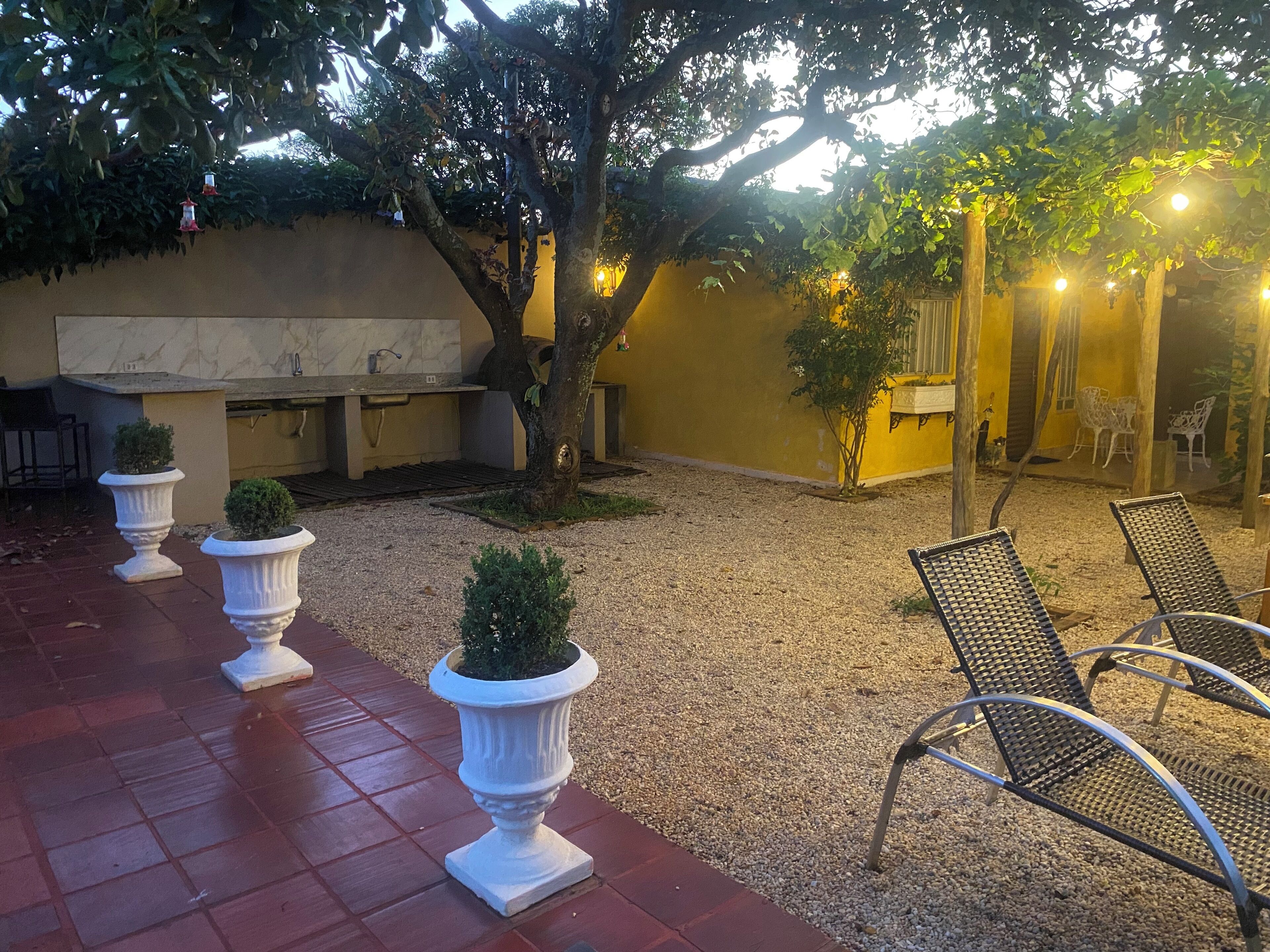Ein Terrassenbereich im Freien mit einer Sitzgruppe, einem kleinen Baum und einer Wand mit einem Fenster.