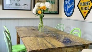 A wooden table with a floral centerpiece, surrounded by green chairs, in a room with framed signs on the wall. - Central Dingle Townhouse (Dingle)