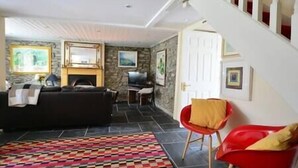 A living room with a black sofa, a red chair, a patterned rug, and a fireplace. - Central Dingle Townhouse (Dingle)