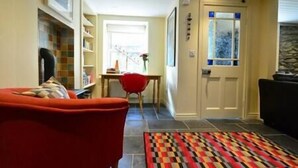 A living room with a red sofa, a patterned rug, a bookshelf, and a door with a window. - Central Dingle Townhouse (Dingle)