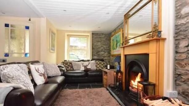 A cozy living room with a fireplace, a stone wall, and a black leather sofa. - Central Dingle Townhouse (Dingle)