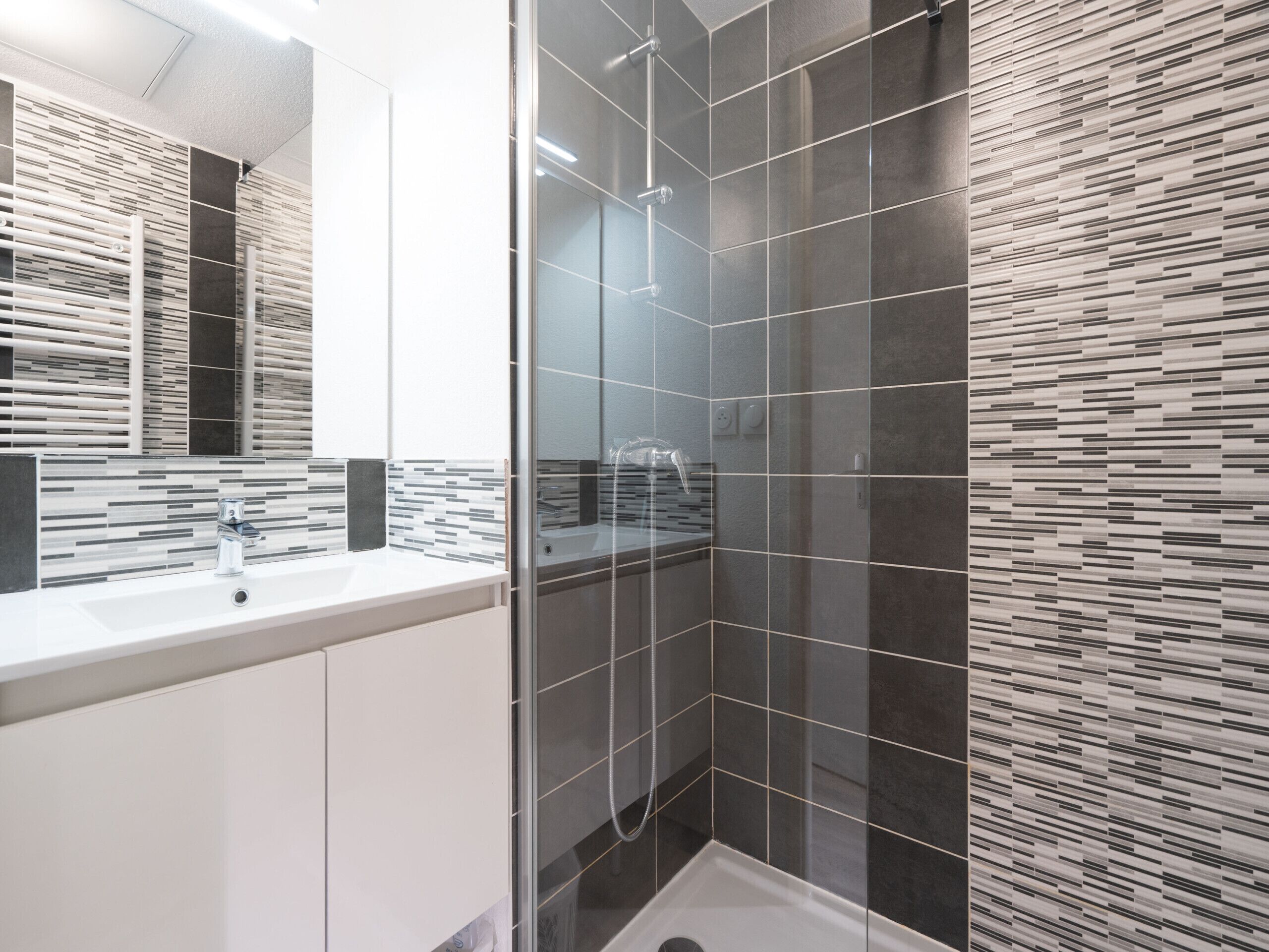 A modern bathroom with a glass shower enclosure, a white sink, and a tiled backsplash.