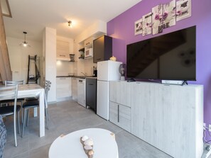 Una cucina moderna con mobili bianchi, una zona pranzo con tavolo e sedie bianche, un grande televisore a schermo piatto montato su un mobile in legno e una parete viola con quadri incorniciati.