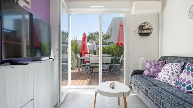 A modern living room with a sofa, a small round table, and a TV on a cabinet. - Air-conditioned Villa, garden, close to the sea (Sérignan)