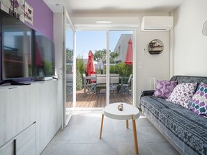 A modern living room with a sofa, a small round table, and a TV on a cabinet. - Air-conditioned Villa, garden, close to the sea (Sérignan)