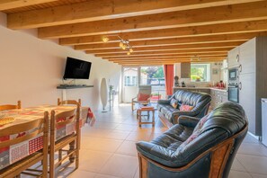 Un salon avec un plafond en bois, un téléviseur fixé au mur, une table à manger avec des chaises et un canapé en cuir.