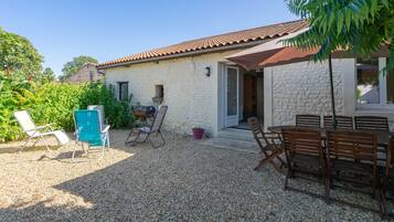 Un bâtiment en pierre avec un toit en tuiles, des places assises à l’extérieur et une terrasse en gravier.