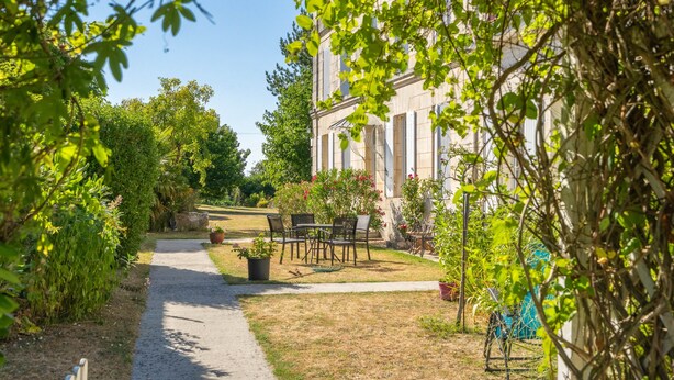 Un camino que lleva a un edificio con jardín, mobiliario exterior y una valla.