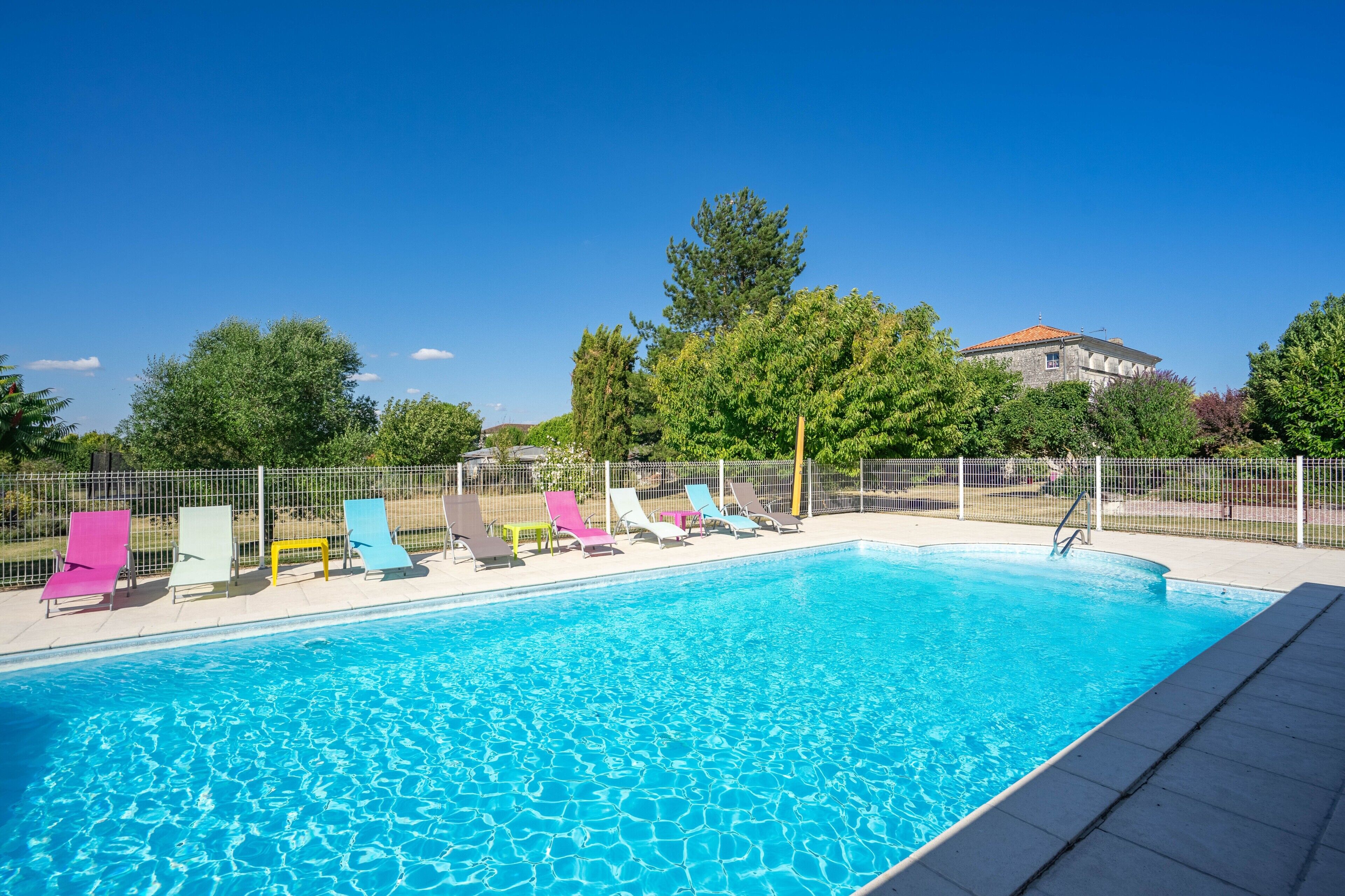 A swimming pool with a tiled deck, surrounded by a fence, and several lounge chairs.