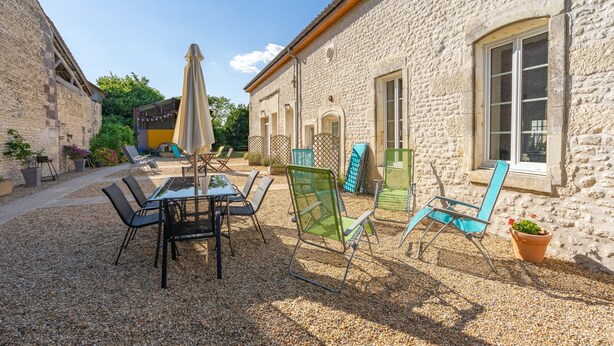A courtyard with a table and chairs, a potted plant, and a building with stone walls and windows.