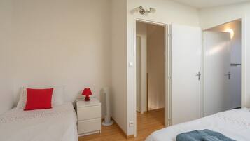 Un dormitorio con dos camas, una mesita de noche con lámpara, un calentador y una puerta que da a otra habitación.