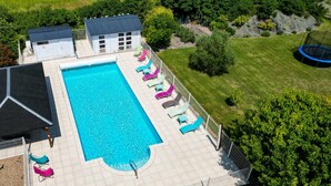 A rectangular swimming pool with a tiled deck, surrounded by lounge chairs and a fenced area.