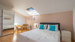 A bedroom with a skylight, a bed with patterned bedding, a nightstand, a chair, and a wardrobe.