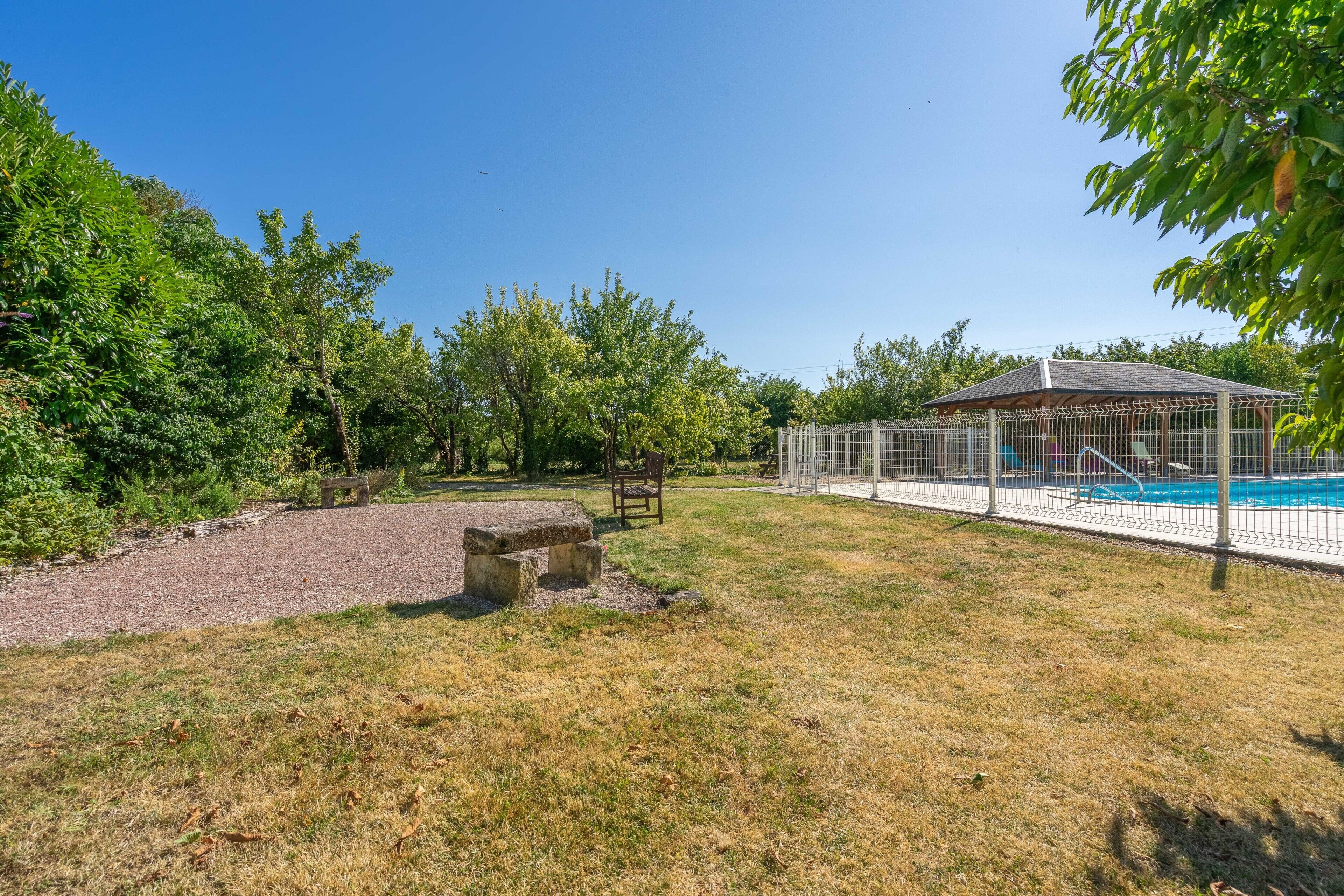 A fenced outdoor area with a pool, a gazebo, and a stone bench.
