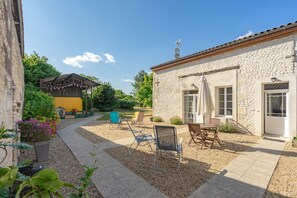 Un edificio de piedra con techo de tejas, un patio con mobiliario exterior y un jardín.