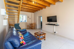 Una sala de estar con un sofá de cuero azul, una escalera de madera, un televisor y un comedor.