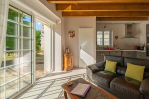 Un salon avec un canapé en cuir, une table basse en bois et une vue sur le jardin grâce à des portes vitrées.