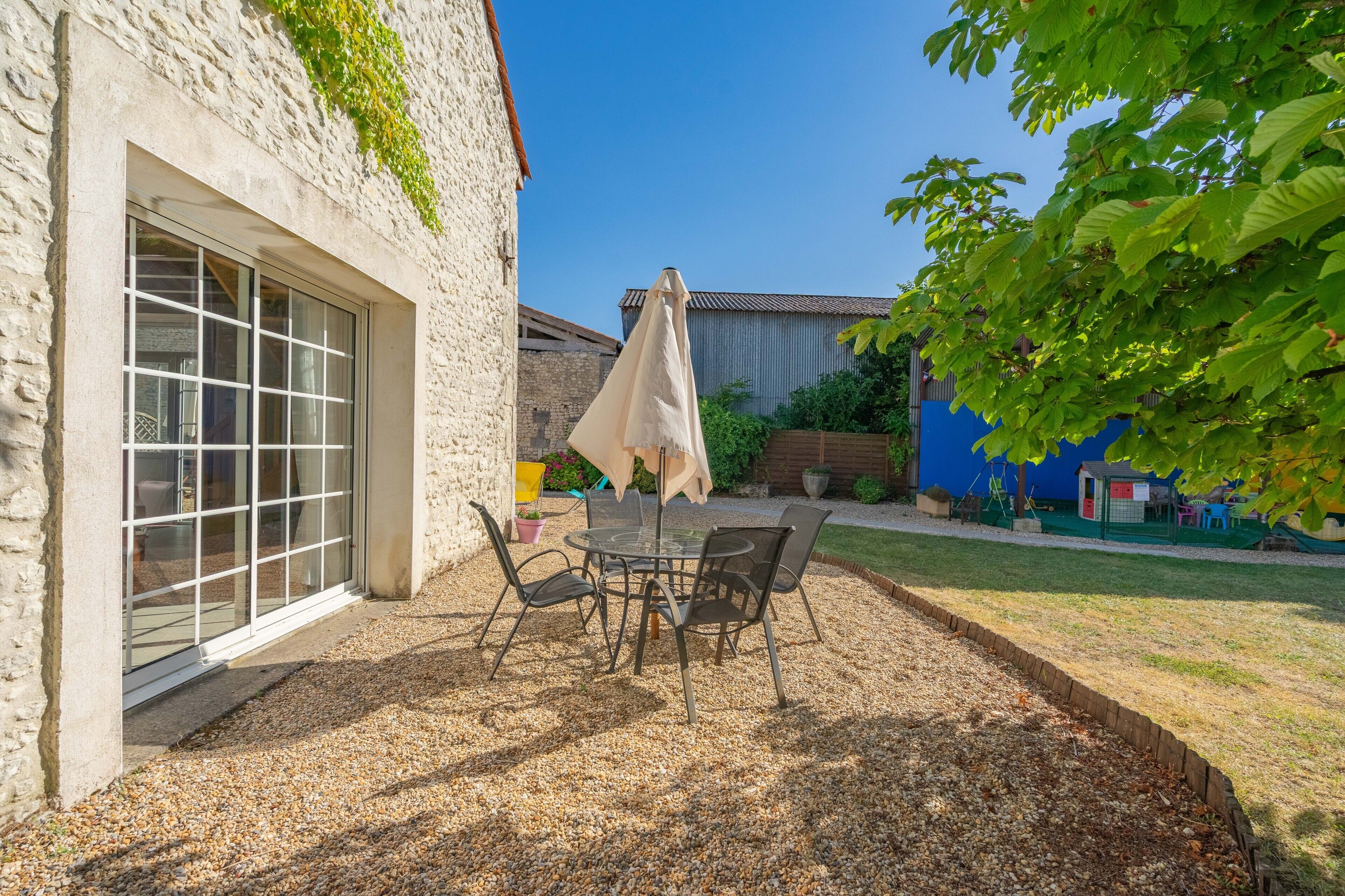 A patio with a table and chairs, a covered umbrella, and a stone building with a window.