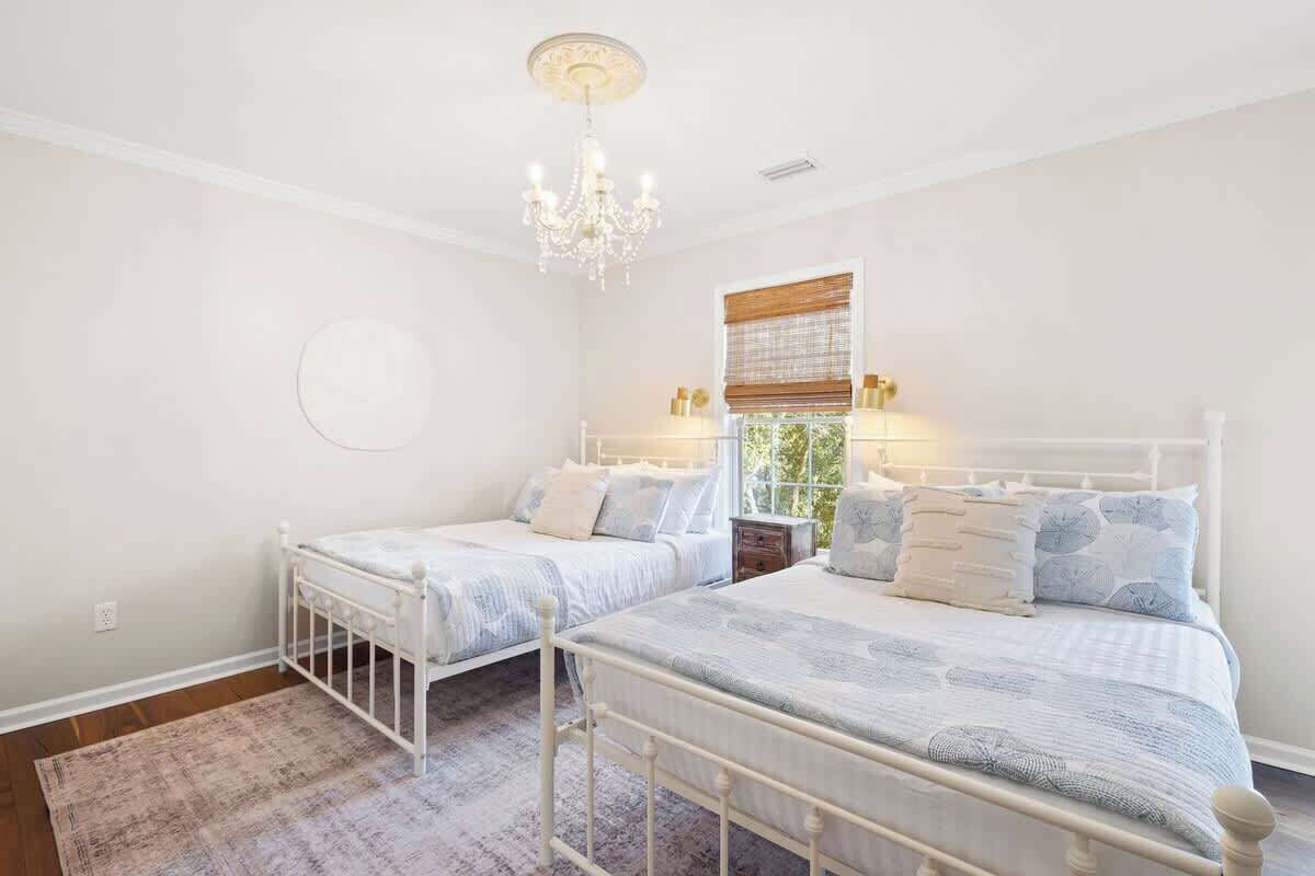 Une chambre avec deux lits, un lustre, une fenêtre avec des stores et un élément décoratif rond sur le mur.