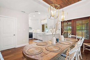 Une cuisine moderne avec des meubles blancs, un îlot central en bois agrémenté de sets de table en fibres naturelles et un luminaire suspendu.