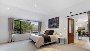 Une chambre à coucher moderne avec un grand lit, une table de chevet, une fenêtre avec des rideaux et un tableau au mur.