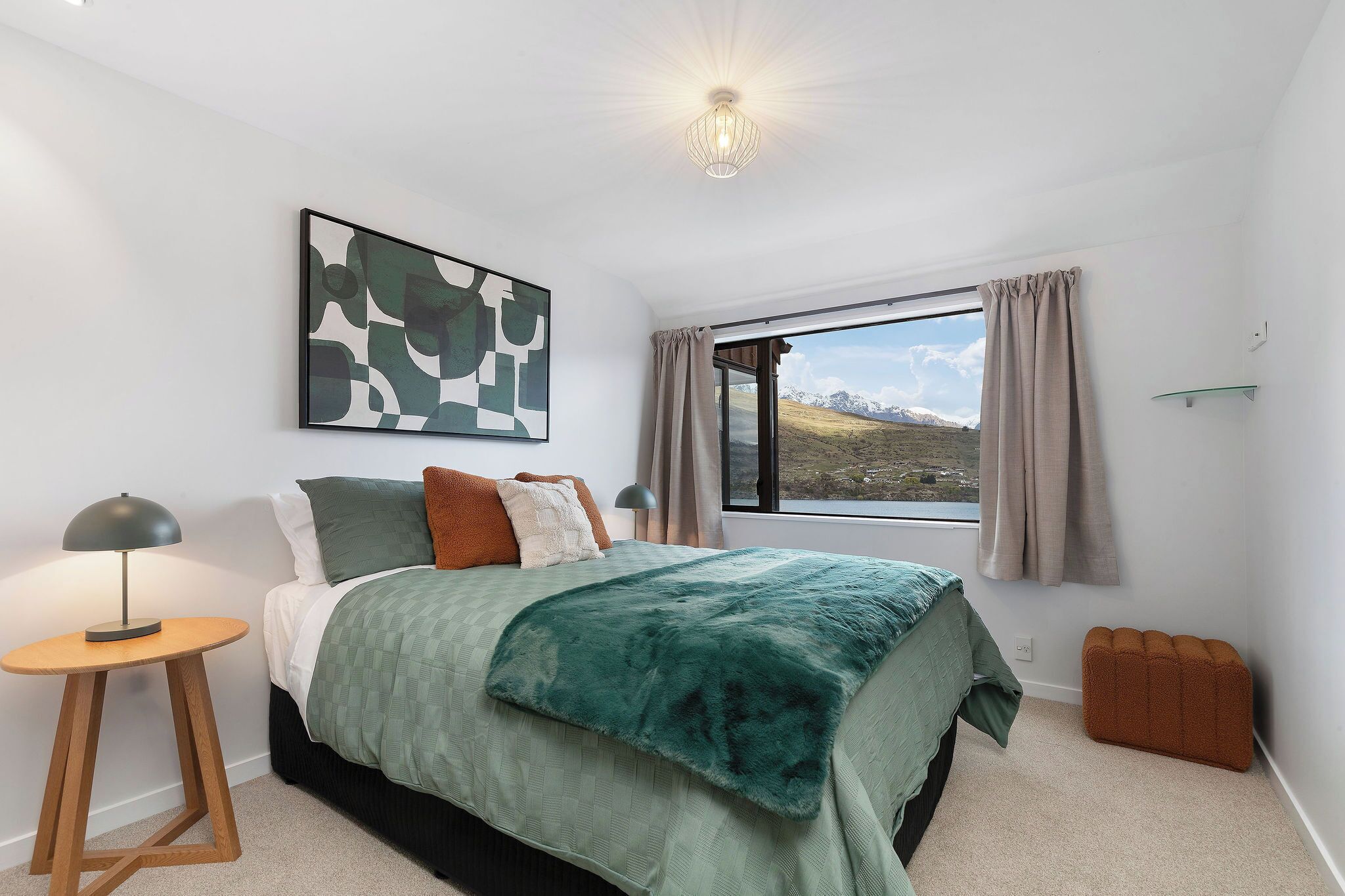 A bedroom with a bed, a bedside table, a lamp, a window with curtains, and a painting on the wall.