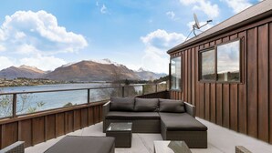 Un balcon avec un canapé, deux petites tables d’appoint et une vue sur les montagnes et un lac.