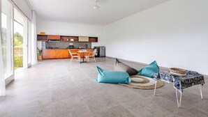 Un grand espace de vie comprenant un coin cuisine à l’arrière-plan, une table à manger avec des chaises et un canapé agrémenté de coussins.