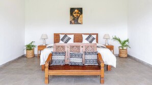 Une chambre à coucher avec un lit en bois, des coussins à motifs, deux tables de chevet et des plantes en pot.