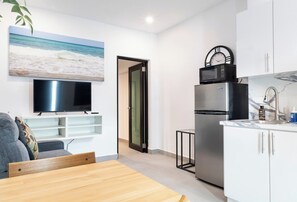Ein modernes Wohnzimmer mit Fernseher, einer Couch, einem Couchtisch aus Holz und einem Gemälde mit Strandmotiv.