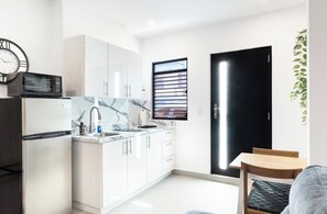 Una cocina moderna con armarios blancos, encimera de mármol, microondas negro y un reloj en la pared.