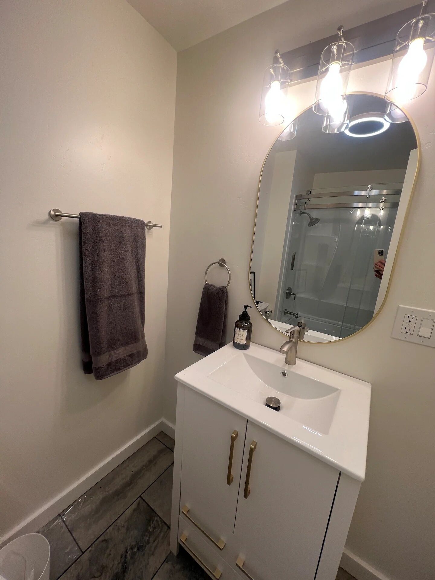 A bathroom with a white sink, a mirror with lights, a towel rack, and a shower.