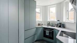 A modern kitchen with teal cabinets, a dishwasher, a stove, and a coffee maker. - Stylish 2 Bedroom / 2 Bath in Notting Hill (London)