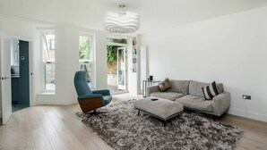 A modern living room with a light-colored sofa, a blue armchair, and a shaggy rug. - Stylish 2 Bedroom / 2 Bath in Notting Hill (London)