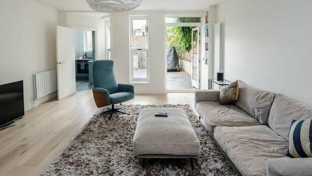 A modern living room with a sofa, ottoman, and armchair, a flat-screen TV, and a fluffy rug. - Stylish 2 Bedroom / 2 Bath in Notting Hill (London)