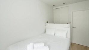 A white room with a bed, a door, and a mirror on the wall. - Stylish 2 Bedroom / 2 Bath in Notting Hill (London)