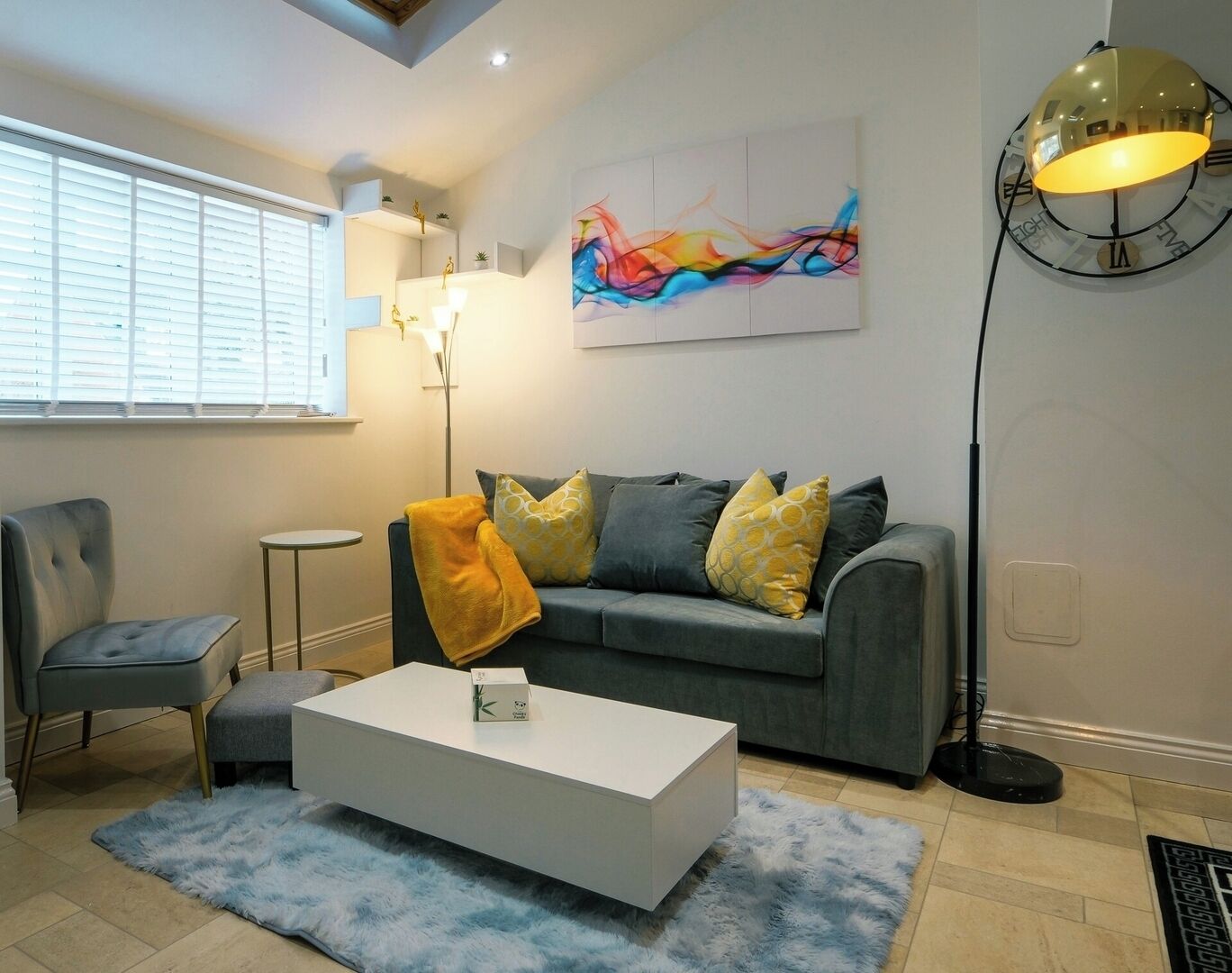 A modern living room with a grey sofa, a white coffee table, and a blue shag rug.