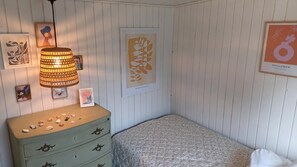 A bedroom with a bed, dresser, wall-mounted lamp, framed artwork, and a poster.