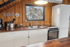A kitchen with wooden walls, a window, a sink, a stove, and a refrigerator.