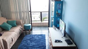 Ein Wohnzimmer mit einer Couch, einem kleinen runden Tisch, einem blauen Teppich, einem Fernseher und einer Vitrine.